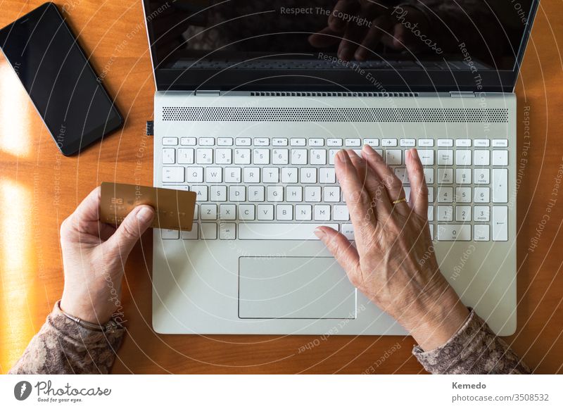 Top view of hands of an old woman shopping online using a credit card and a laptop at home. Concept of old people and technology. pay elderly computer