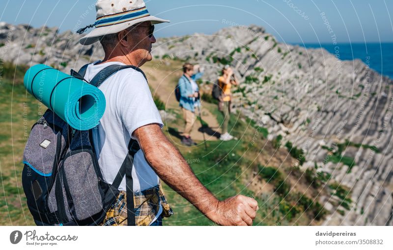 Senior man trekking looking at the landscape hike senior mountain mat backpack nature hat sunglasses countryside backwards summer hikers retired pad sea ocean