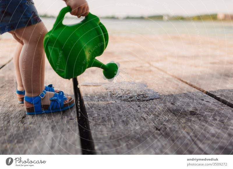 A small girl is playing with a watering can of a wooden bridge. Spring and summer. Gardening. green watering can baby little child cute garden background white