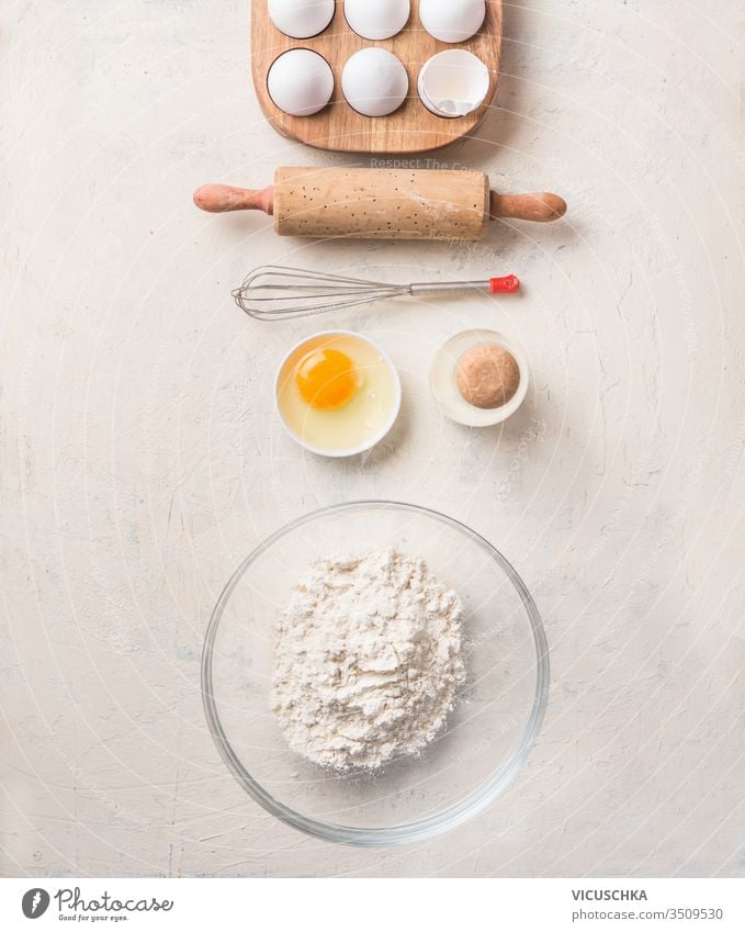 Baking tools and ingredients for cookies, pie or cake bake on white background. Top view. Flat lay. Flour in glass bowl, eggs in wooden holder, vintage rolling pin and whisk.