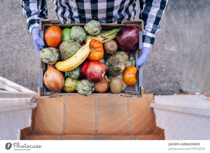 Male volunteer holding a box with vegetables and fruits in a house stairs. Volunteer,lockdown,epidemic concept aid assist assistance charity community