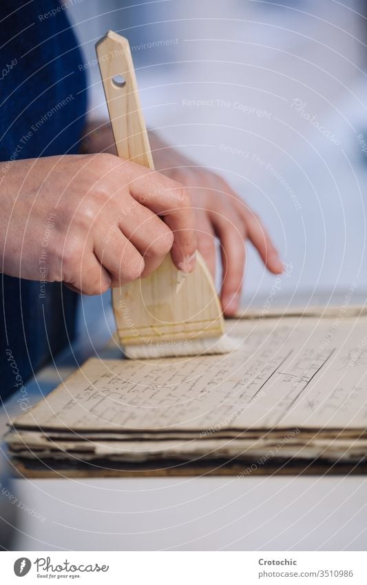 Person cleaning a page of an old book with a brush to repair it ancient hand person worker soft care vertical bookbinding wood handcraft handmade paper printing