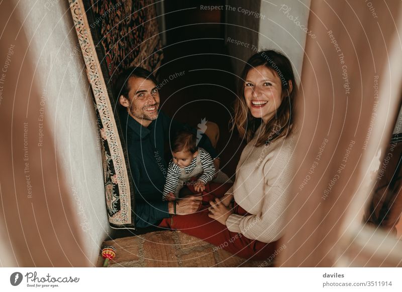 Cute family of Handsome man and beautiful woman sitting on the stairs at home, while play with their baby son, looking at camera. handsome white holding smiling