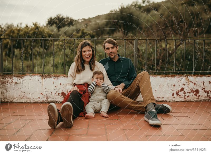 Happy family portrait with man and woman sitting on the floor with their baby at home terrace. real authentic alternative patio cheerful wife carefree backyard