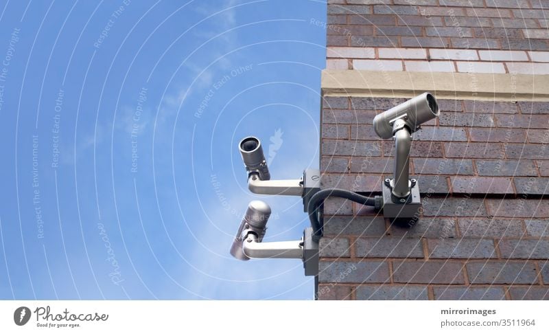 corner of an outdoor brick building with 3 csurveillance camera poiinting in different directions on a beautiful day cctv city control electronic equipment lens