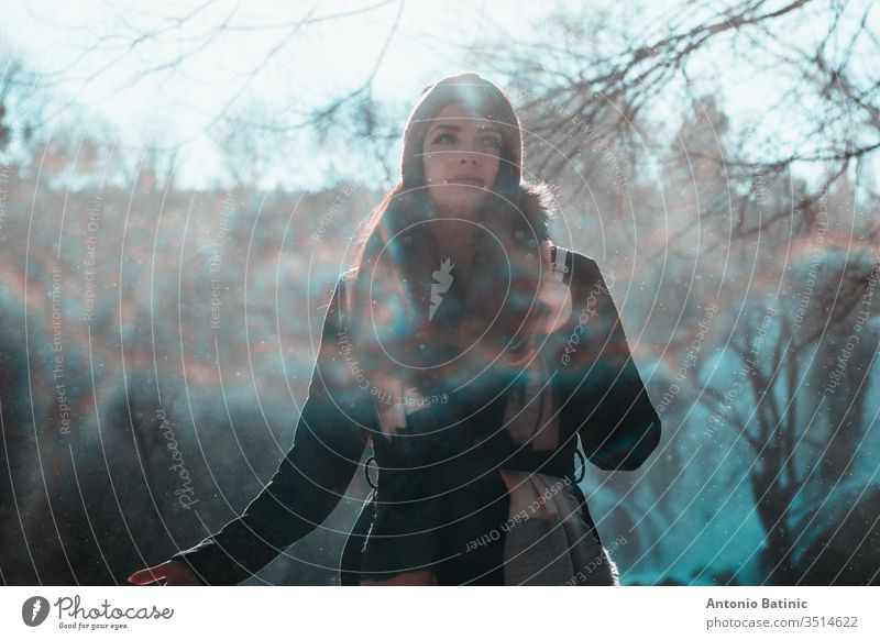 Attractive brunette in winter clothing and an orange head scarf posing on a cold winter day looking into the distance. Water droplets flying everywhere creating a mist,fog and mini rainbows