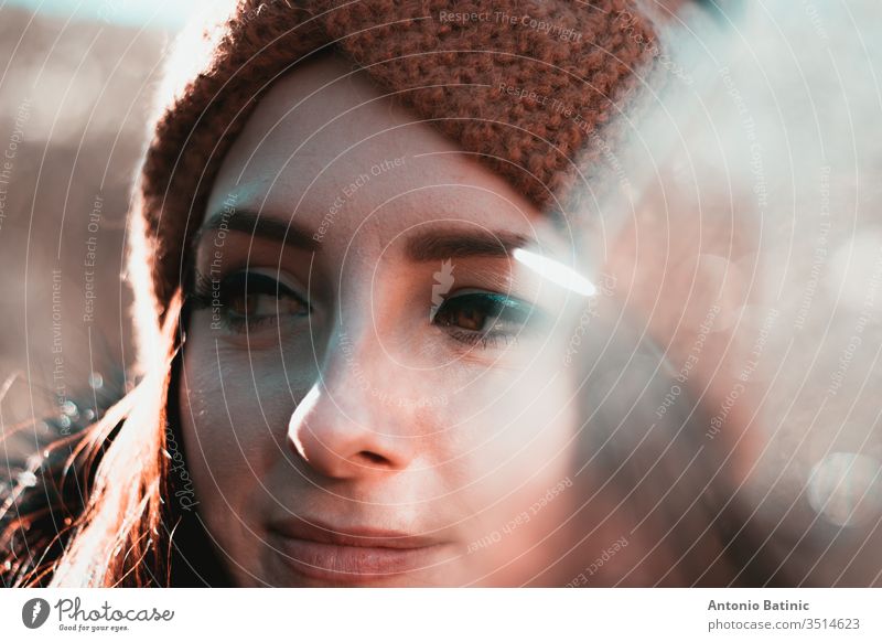 Closeup headshot of an attractive brunette in winter clothing and an orange headband. Cold winter day in the forest, serious happy face looking into the distance thinking