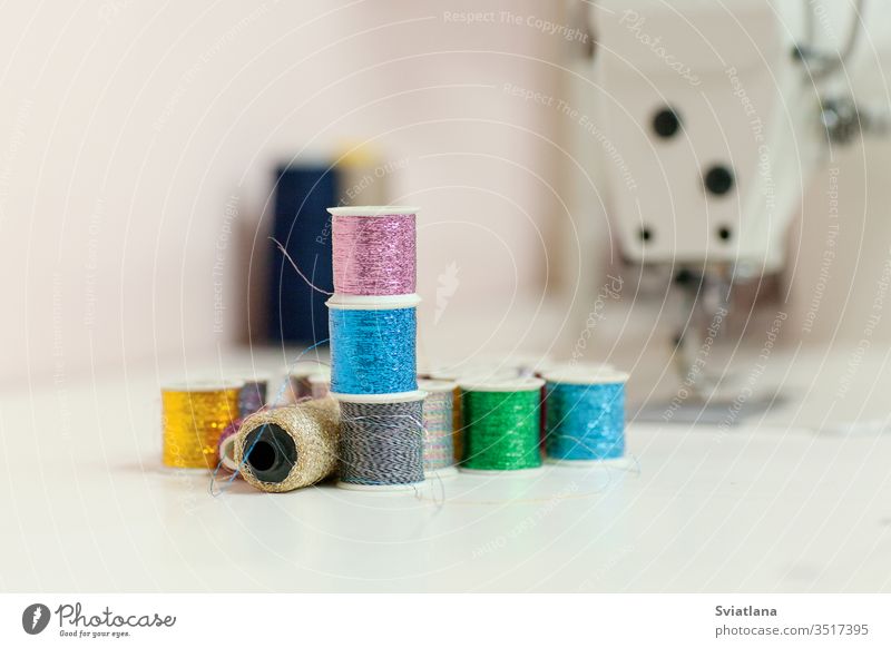 Sewing accessories on the desktop close-up. Sewing threads from lurex in spools, in the background a sewing machine chalk table sewing set reel red yellow