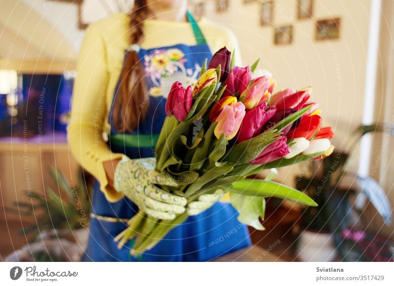 The seller holds a large beautiful bouquet of tulips packed. Side wiev hands paper kind pink packaging floral market scissors spring gloves ribbons rope