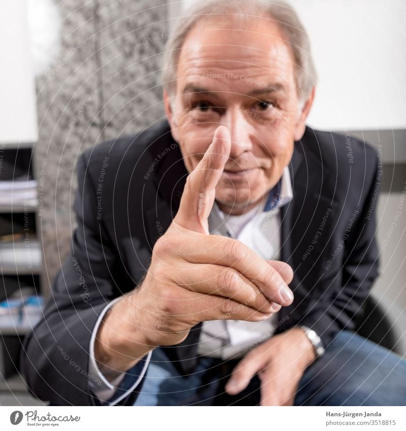 Older man in a suit raises a finger smiling Man Businessman civil servant Chair Armchair Senior citizen by hand Fingers smile central Warn Suit chief Shirt Face