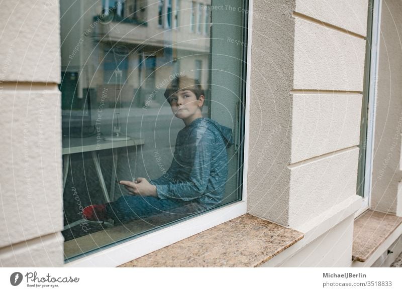 Boy sits lonely at the window and looks at his mobile phone during lockdown isolation in the coronavirus epidemic Boy (child) Child Lonely Loneliness by oneself