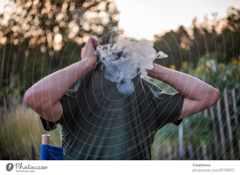 The young man in the garden pulls his T-shirt over his smoking head on a summer evening Smoke Smoking Man Tobacco Addiction Nicotine Tobacco products Dependence