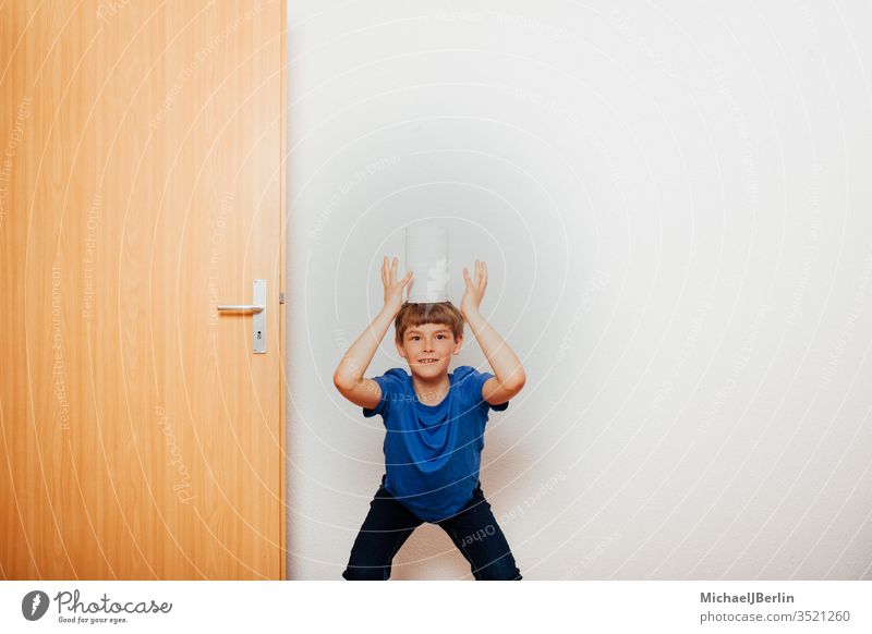 Boy balances toilet paper on his head left Toilet paper Balance Boy (child) Child Corona covid-19 Epidemic fun game Hoarders Hoarding Home Outbreak pandemic