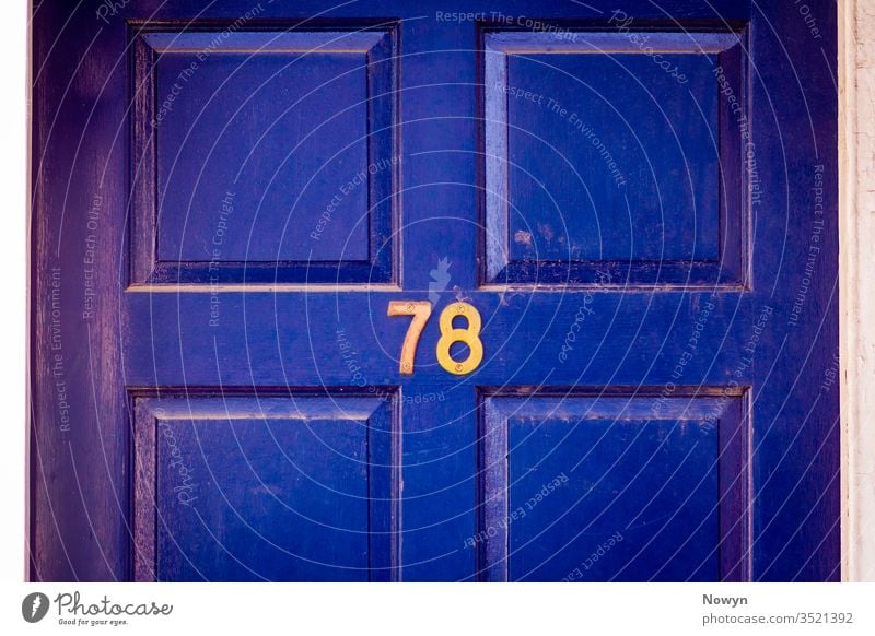 House number 78 on a dark blue weathered and worn wooden front door 78 number address britain classic classy close up closeup decoration design detail digit