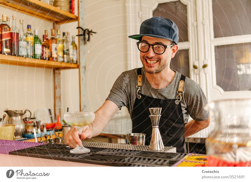 Waiter showing an ice-cold glass with a cocktail prepared at the bar of a modern bar serve ready alcohol smile transfer liquid glasses mint frost apron waiter