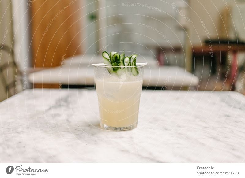 White liquor cocktail with some cucumber pieces to decorate served on a marble table in a bar white chair mixed refreshment shake smooth vegan drinking health