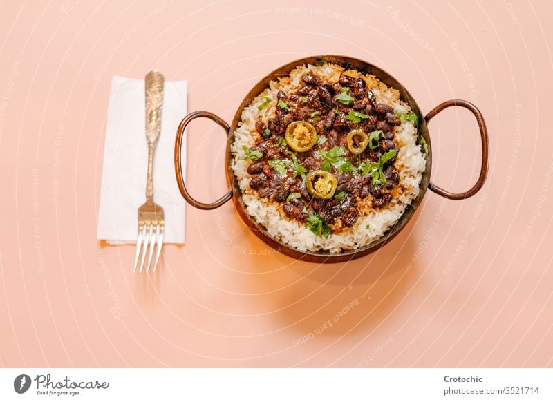 Aerial view of a pan with rice and beans decorated with chopped green chilies and served on a wooden table fork napkin ready hot decoration pepper design black