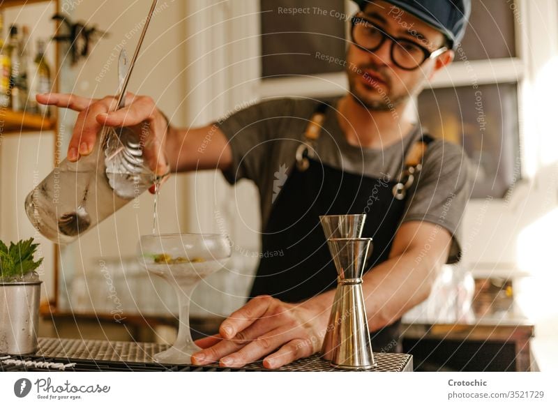 Waiter transferring liquid into a glass with ice to a frost cocktail glass alcohol bar pouring glasses mint apron waiter hotel fresh restaurant measure mixed