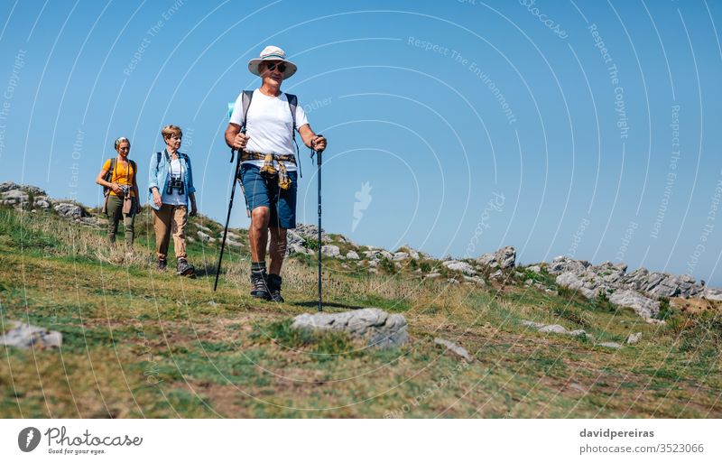 Three people practicing trekking outdoors hikers local tourism family countryside walking trekking sticks senior nature nordic walking summer landscape