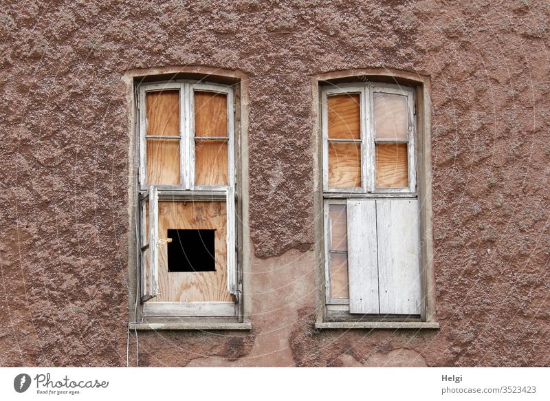 old | facade of an old building with broken windows closed with boards, one has a peephole Facade built Manmade structures Window locked open Broken Nailed down