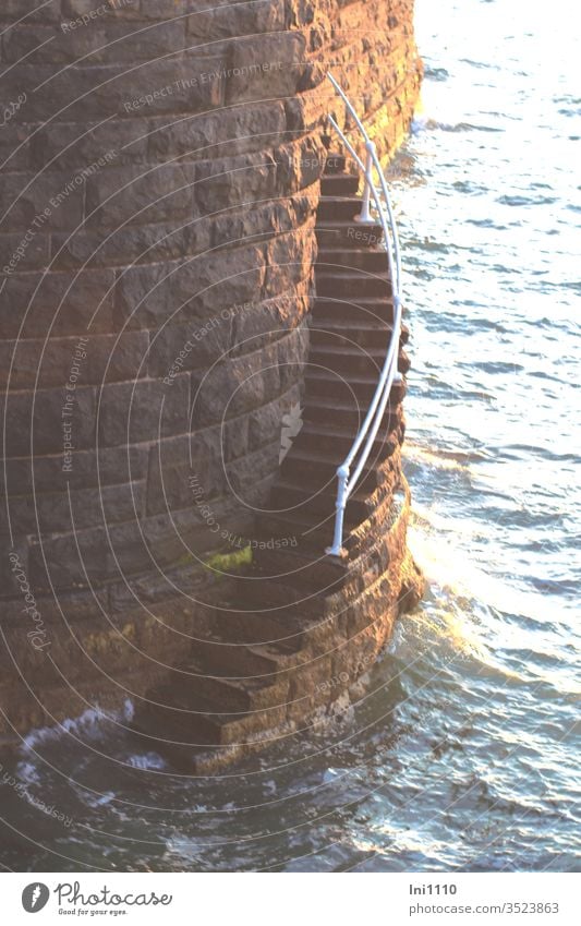 slightly curved narrow stone staircase with railing leads down to the sea in the evening light at the quay wall Steep Deep Narrow Handrail Dangerous