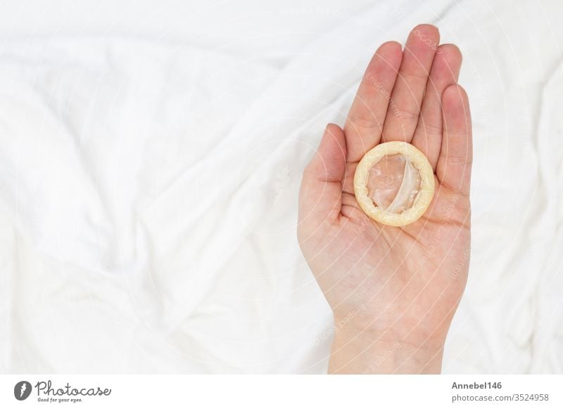 Safe sex concept. Hand holding a condom with white sheets blanket background hand protection aids healthy control contraception contraceptive hiv man safe