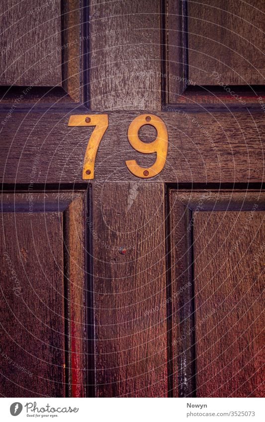 House number 79 on a dark wooden front door 79 number address aged britain classic classy close up closeup decoration design detail digit digits elegance