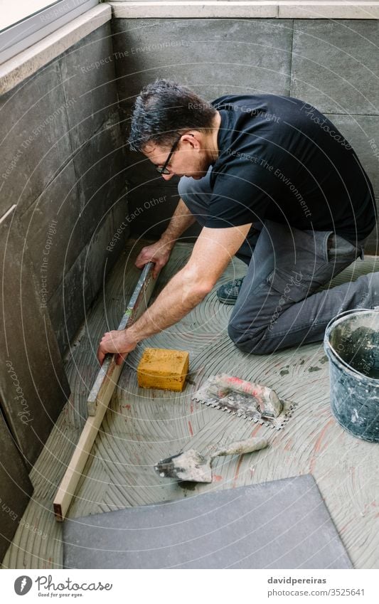 Bricklayer checking floor with a level mason workman leveling ground tiling renovation make sure imitation cement tile glazed terrace verifying working