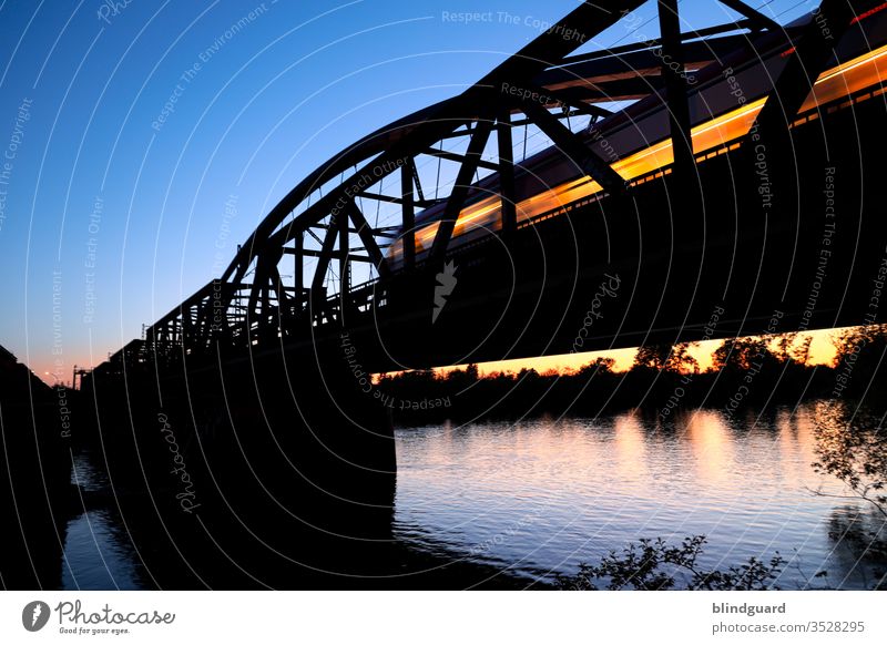 The last night train begins its long journey. Train with illuminated windows crosses the Main in Hanau at sunset on the Steinheim Bridge Railroad Rail transport