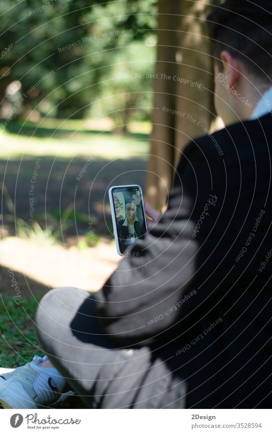 Back view of a young teenage student sitting on campus while using a mobile phone person technology lifestyle smartphone communication teenager holding outdoor