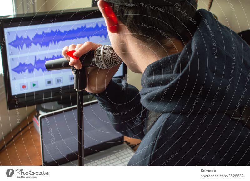 Back view of a man singing in a microphone and recording the audio to make a song at home. Amateur musician singing and playing guitar. quarantine coronavirus