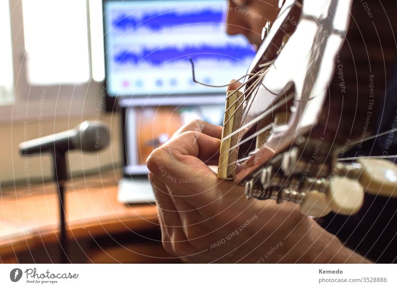 Person playing guitar and recording the audio using microphone and technology at home. Amateur musician recording music. hand man close up blur enjoy focus