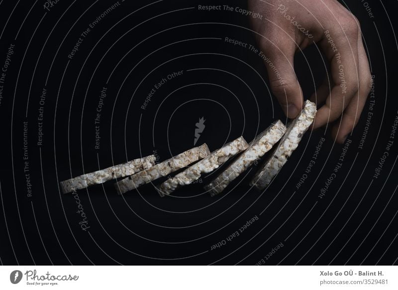 Puffed Rice Slices arranged like a domino chain on black background, the last held by a hand Hand holding puffed rice gluten free Healthy Lifestyle