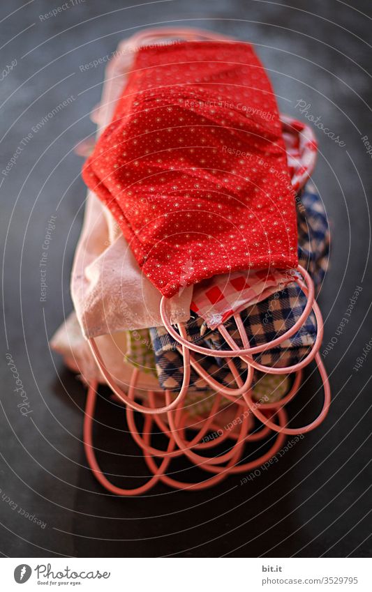 Many, colorful, self-sewn masks made of fabric to protect against corona, viruses, diseases and against smog, lie in a pile on a black background of a blackboard.