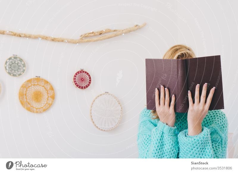 Young woman sitting in bed while reading a book girl coffee sweaters white beautiful morning home bedroom blonde wall lights dreamcatcher sunday young relax