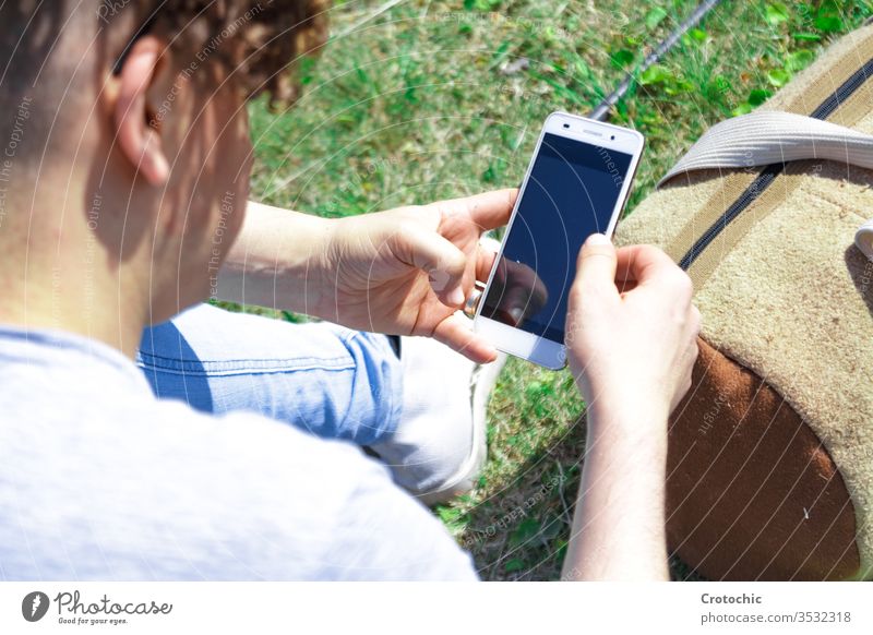 Man using a mobile phone sitting on the grass with a sports bag screen reflection device back detail zoom texting chatting lying lean relax break data