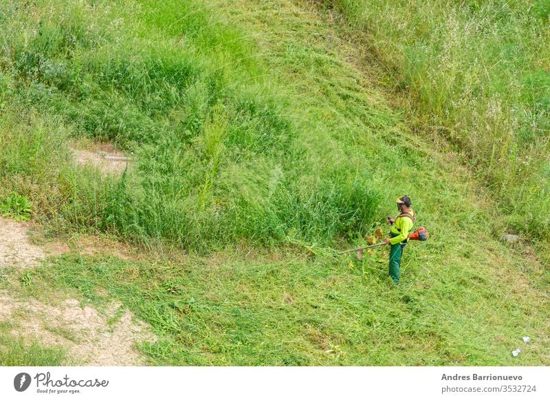 Man in working clothes and equipped with a professional brushcutter cutting the green grass of a solar power outdoors portrait blade tree occupation young adult