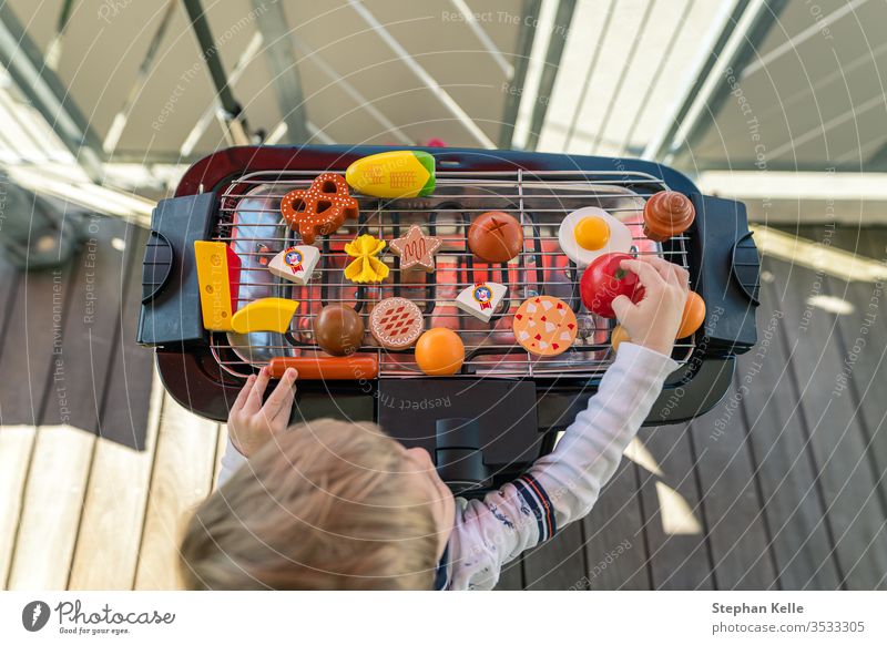 A little boy starts grilling by playing with his vegetables and sausage food toys at the balcony. He is creating a delicious meal for his family. barbecue bbq