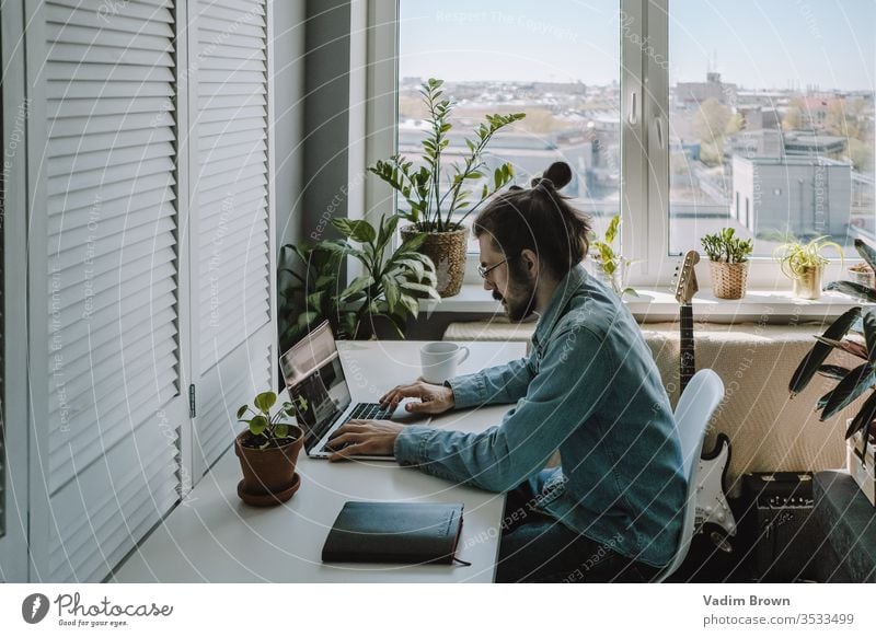 Young man with beard sitting on the chair and using laptop. Freelance work from home in quarantine concept video chat online shopping using technology