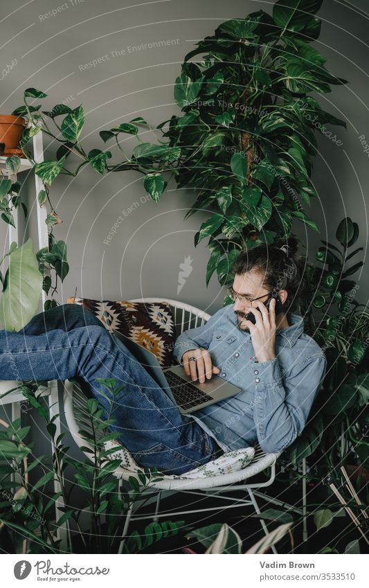 Young man with beard sitting at the table and using laptop home phone work work from home using technology online shopping video chat