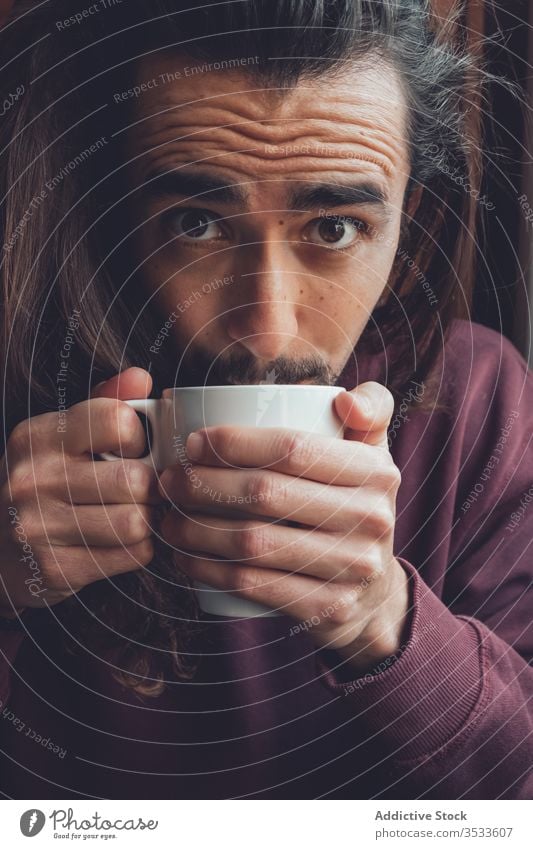 Bearded man resting with hot beverage drink home stay at home coronavirus covid-19 cozy mug mood adult room male relax tea coffee cup comfort long hair beard