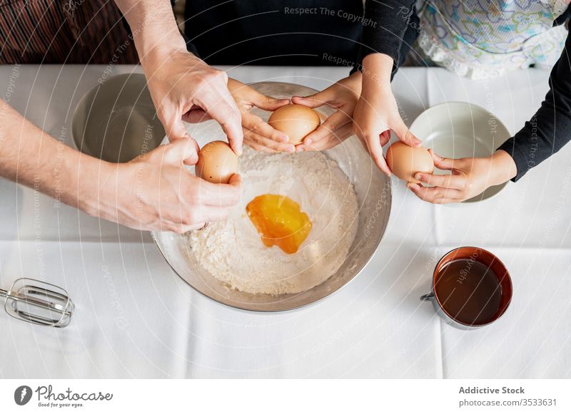 Crop parent and kids adding ingredients during pastry preparation children cook bowl egg crack kitchen home together sibling raw flour metal lifestyle dough