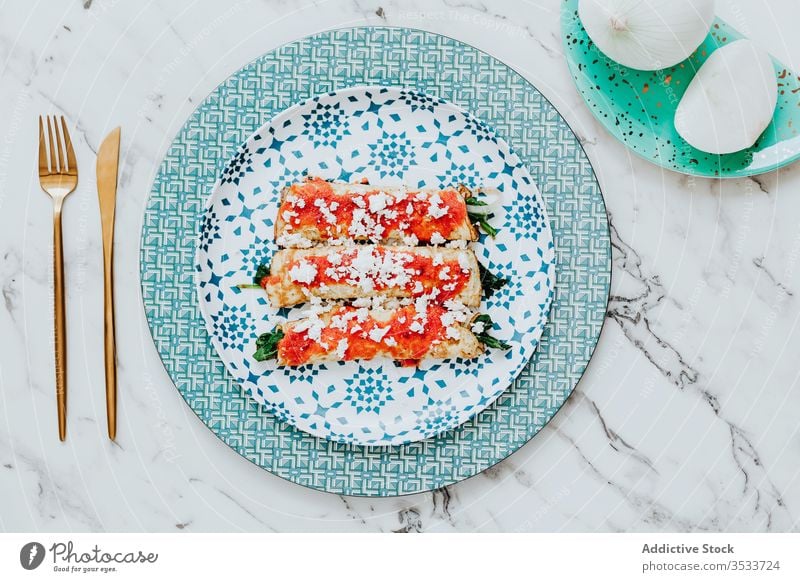 Yummy pancakes with greens and tomato sauce in composition with fresh onion beside cutlery on table roll food meal wheat burrito healthy snack arugula natural