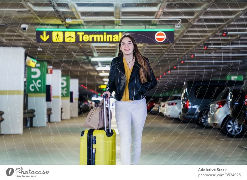 Trendy female passenger walking along airport parking woman traveler suitcase carry joy luggage smile bag trip flight wait journey tourist arrive terminal