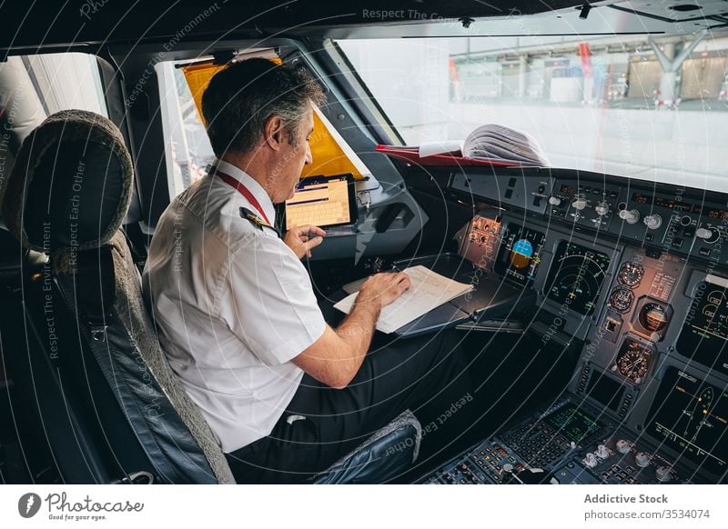 Captain checking flight document in airplane cockpit pilot read captain prepare man aviator male modern aircraft transport aviation departure work occupation