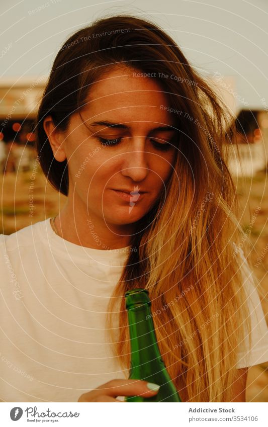 Young lady with bottle of beer during sunset on seashore woman traveler smile refreshment summer chill leisure happy ibiza spain sunglasses drink vacation