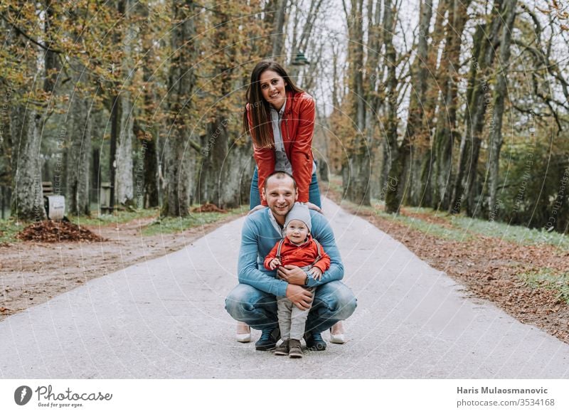 Happy family stylish couple with 1 year old child smiling in the park in red and blue clothes beautiful care caucasian cheerful childhood concept cute dad daddy