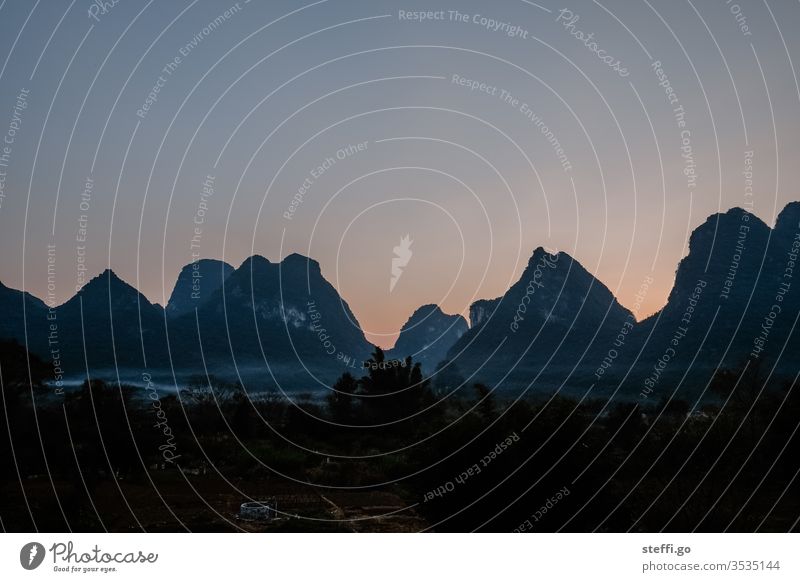 View of mountain range with fog at dusk in Yangshuo, Guilin China Asia Guilin Mountains karst karst landscape karst mountains Mountain range Fog Shroud of fog