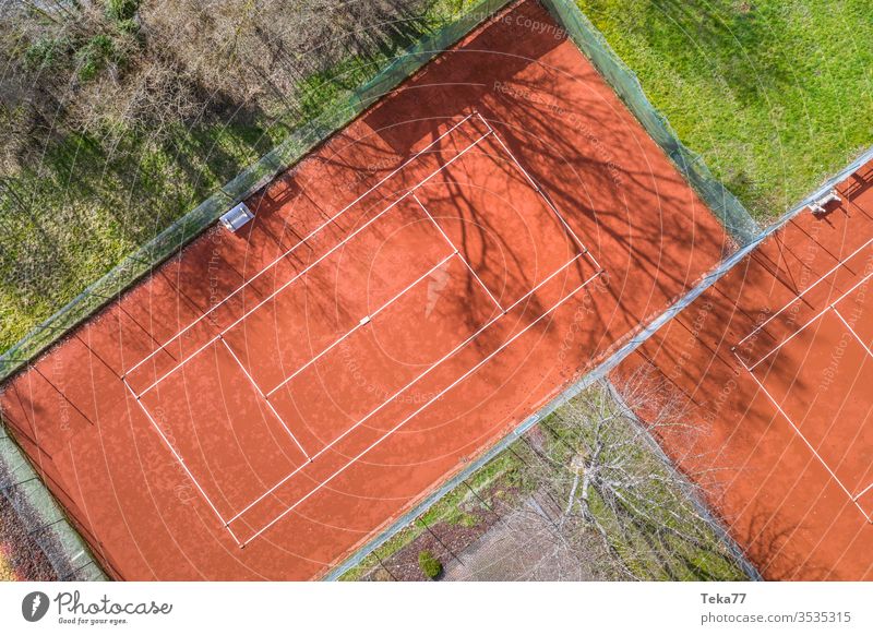 a tennis court from above sport sports tennis courts ash orange white lines sun shadow summer winter sharp tennis net tennis nets ball balls tennis ball trees