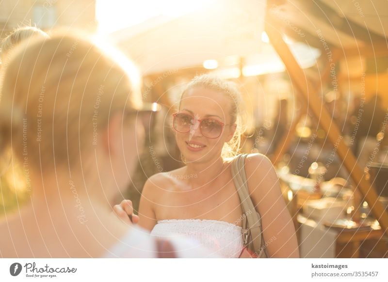 It is nice to see you. It has been a while. Two happy young female friends enjoying a conversation on urban food market at random after work encounter. Pleasant free time socializing